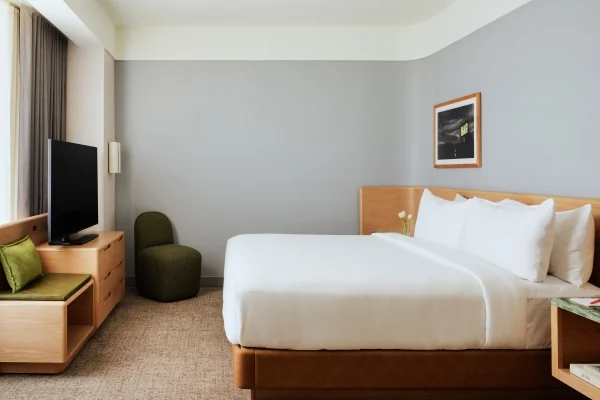 Hotel room with a large bed, white linens, wooden headboard and furniture, gray walls, a framed photo, and a TV on a wooden stand near a window with curtains.