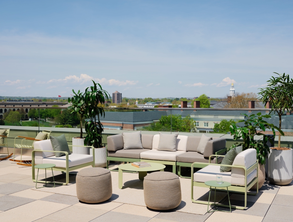 Rooftop patio featuring lounge chairs and sofa, a variety of green potted plants, overlooking the surrounding city skyline.