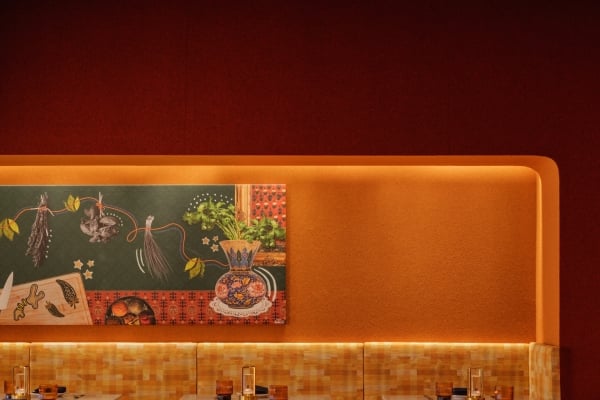 Two seater dining tables with booth seating along a backlit orange accent wall, and black rattan chairs positioned across a marble table.