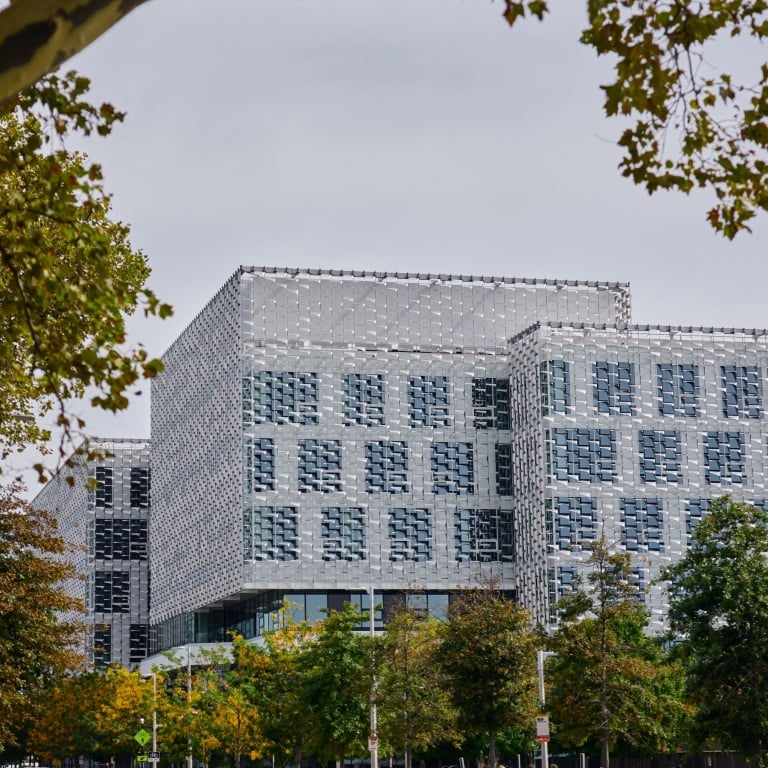 A wide view of the Science and Engineering Complex (SEAS) at Harvard, a large, modern building with a distinctive, patterned exterior facade of metallic panels, framed by trees with fall colors.