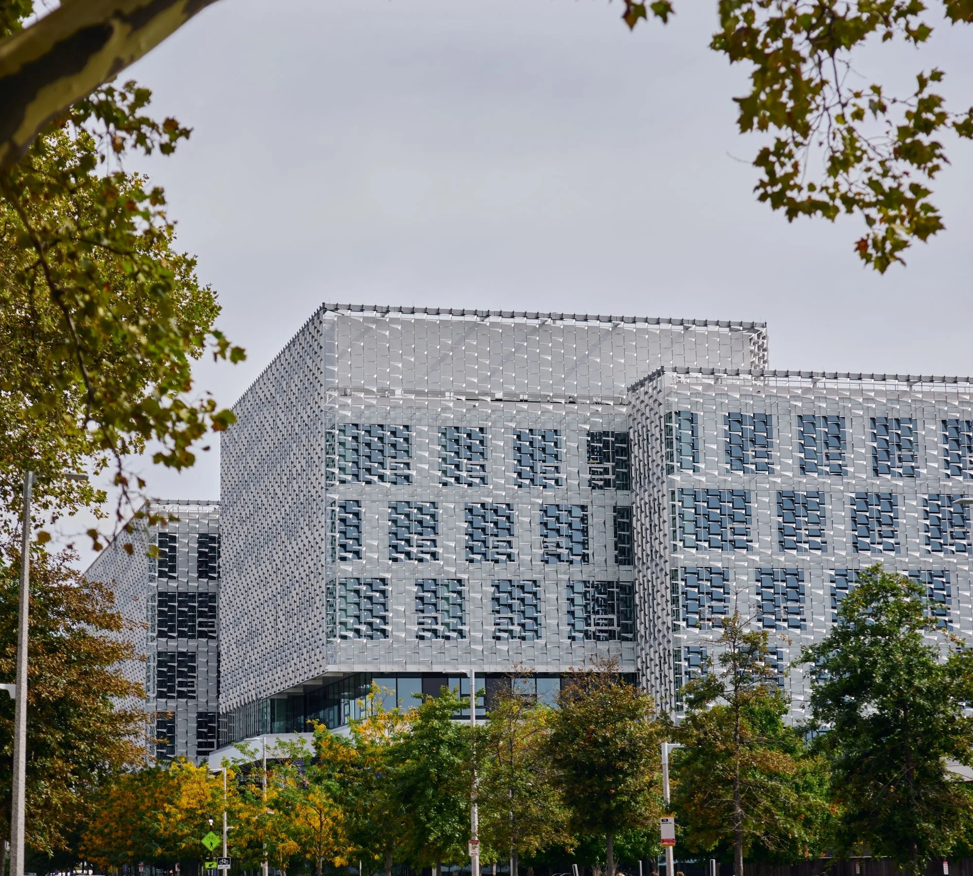 A wide view of the Science and Engineering Complex (SEAS) at Harvard, a large, modern building with a distinctive, patterned exterior facade of metallic panels, framed by trees with fall colors.
