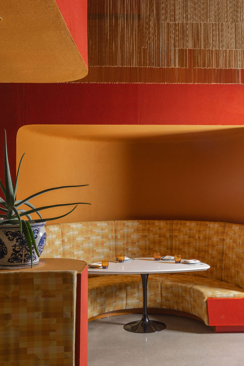 A curved woven booth in warm amber tones surrounds a white table, creating a cozy dining nook.