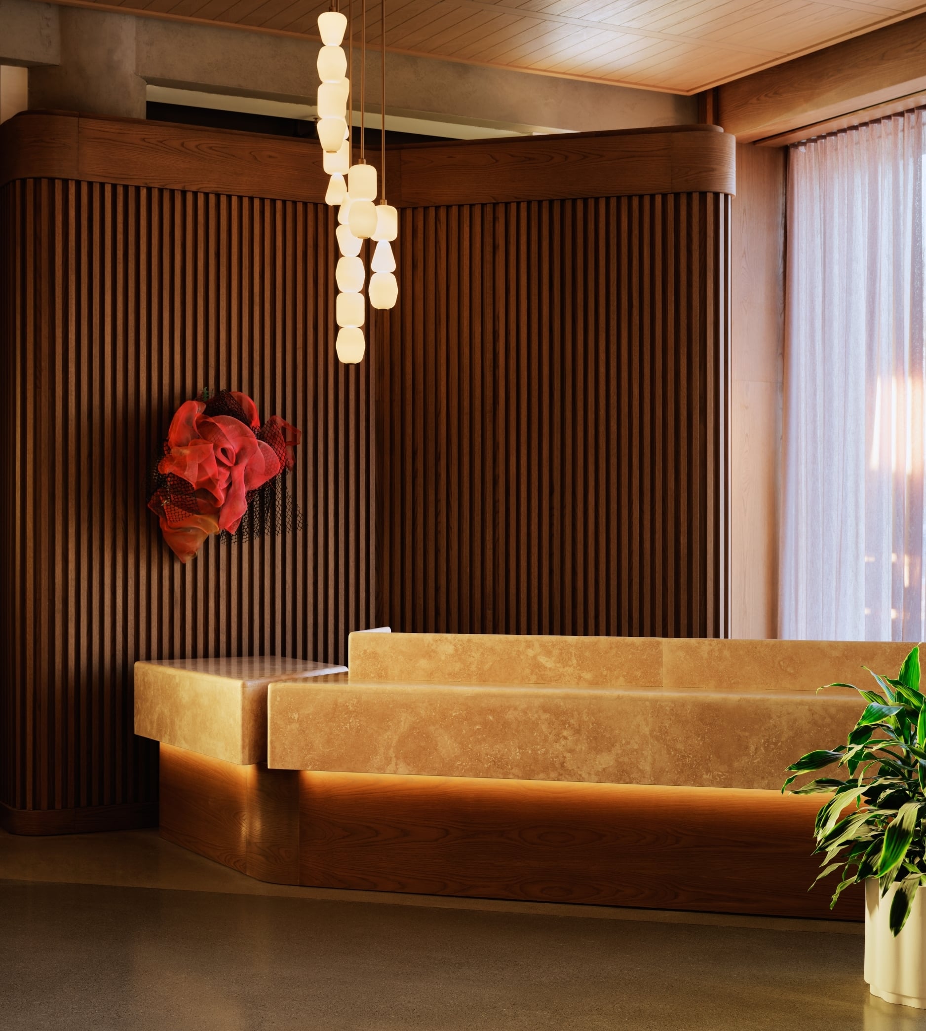 The Atlas front desk in travertine stone beneath stacked pendant lights, with fluted wood paneling and a sculptural red wall artwork.