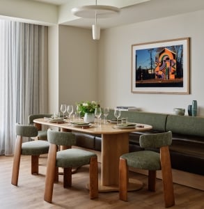 Suite dining area with an oval wood table, green boucle chairs, a built-in bench, and a vibrant street art photograph above