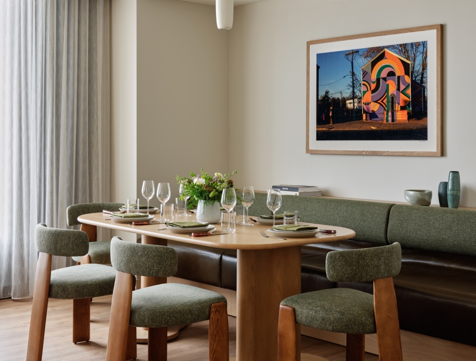Suite dining area with an oval wood table, green boucle chairs, a built-in bench, and a vibrant street art photograph above