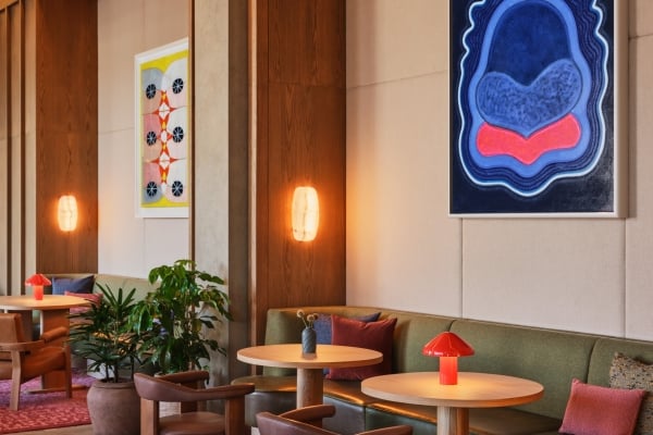 Atlas Hotel seating area with green banquettes, round wood tables, orange mushroom lamps, and bold abstract artwork on the walls.