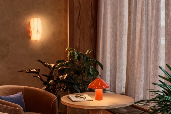 A warm lounge nook with armchairs, a round wood side table, an orange mushroom lamp, and a glowing alabaster wall sconce.