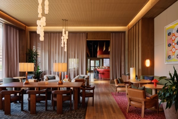 The Atlas hotel lobby lounge with warm wood paneling, pendant lighting, leather seating, and a glimpse of the red bar in the background.