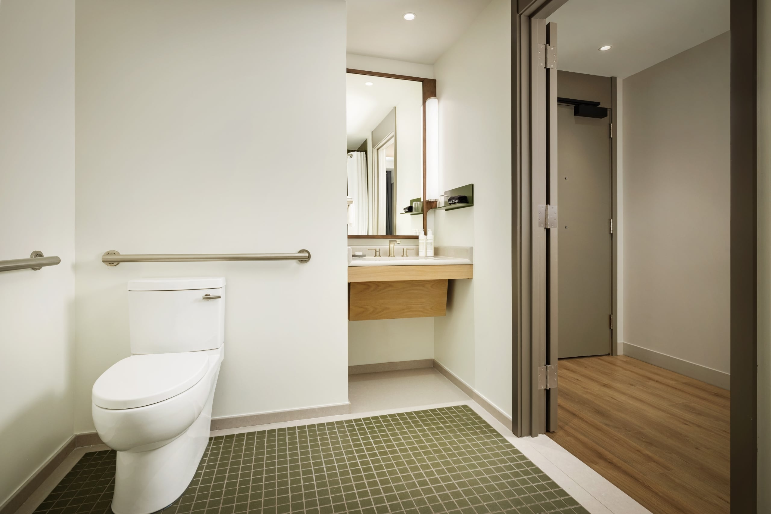 Public bathroom with a white toilet, grab bar, and sink in a clean, well-lit space.