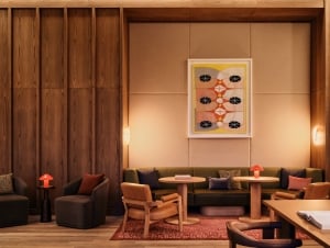 Cozy lounge area with wood-paneled walls, a beige cushioned backdrop, and a framed abstract painting among round tables and plush seating.