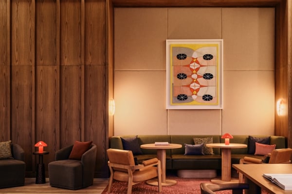 Cozy lounge area with wood-paneled walls, a beige cushioned backdrop, and a framed abstract painting among round tables and plush seating.
