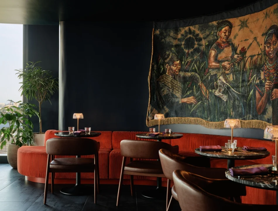 Restaurant seating area with red curved booths, round tables, glasses, and a large fabric mural on the wall.