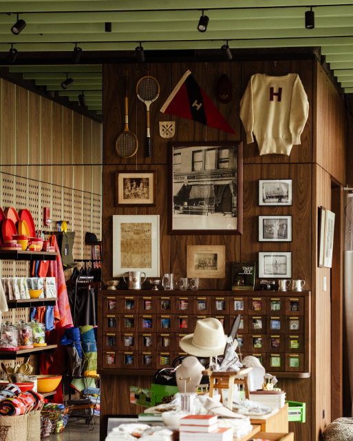 Shop interior with vintage sports memorabilia on a wood wall: rackets, hats, flags, and framed photos.