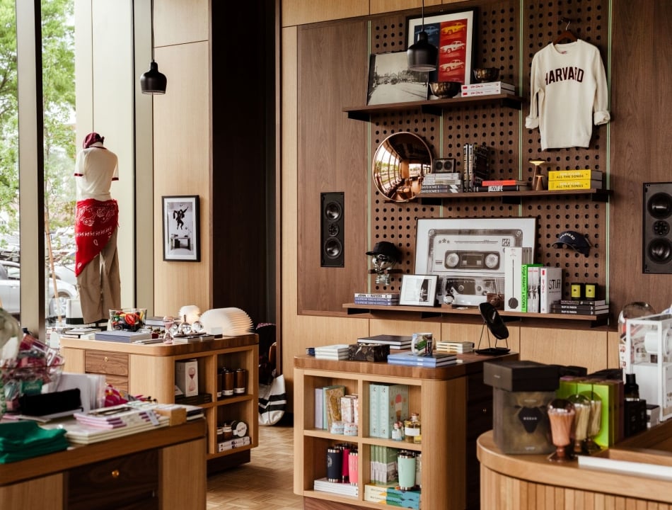 Boutique interior with wooden shelves, a Harvard sweatshirt on display, and a mannequin by the window.