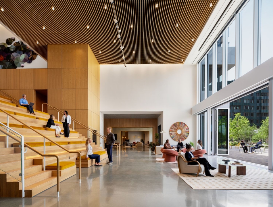 Spacious modern lobby with wooden stepped seating, people chatting and working on laptops at different levels.