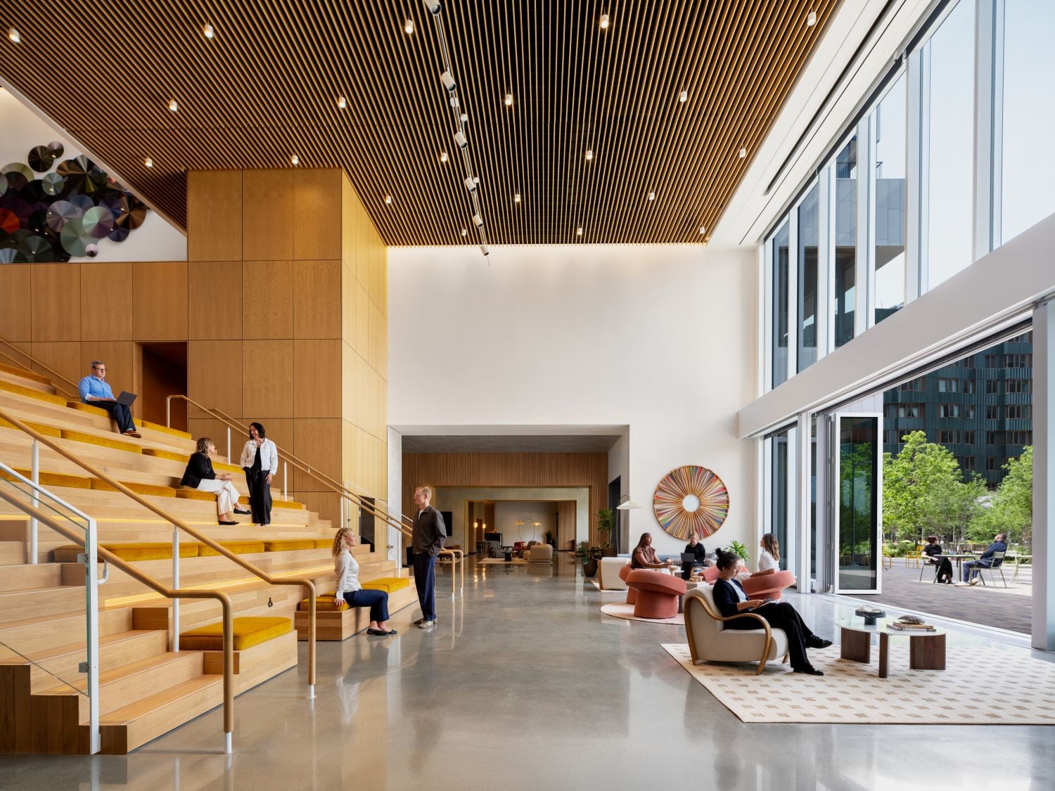 Spacious modern lobby with wooden stepped seating, people chatting and working on laptops at different levels.