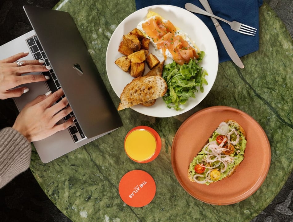 Overhead view of a person typing on a laptop at a green marble table with two plates of food and orange juice nearby