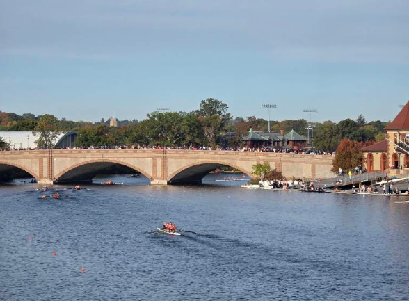 Stone arch bridge over a wide river with many people on the walkway and rowers on the water.