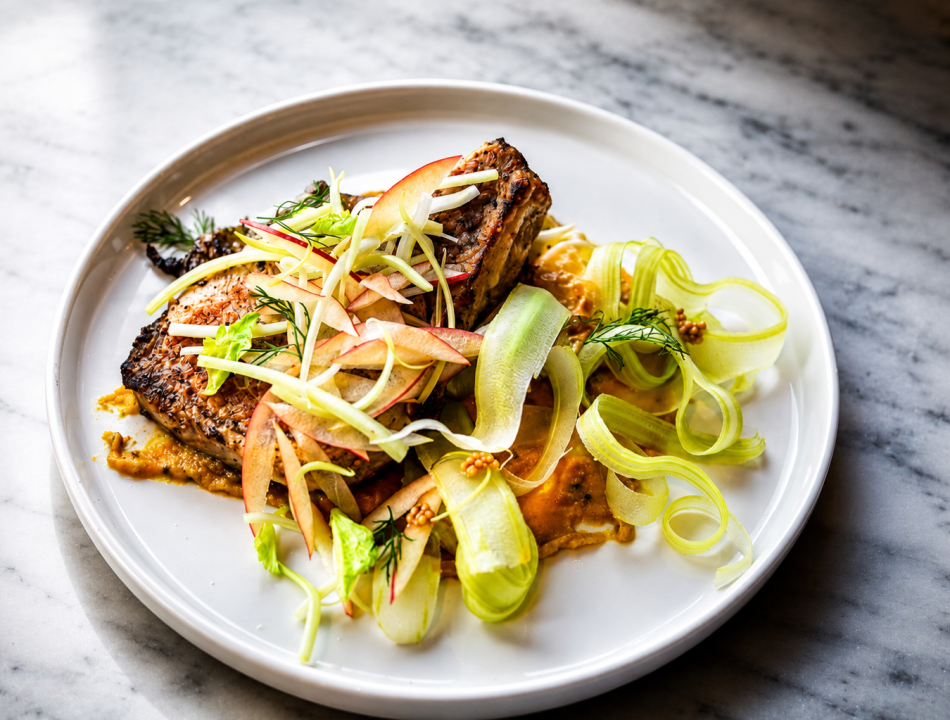 Seared salmon fillet with crispy skin, topped with apple‑fennel slaw and dill on a white plate.