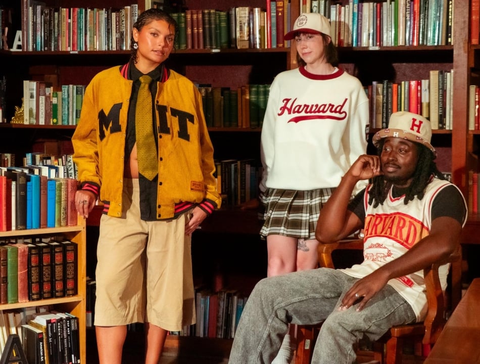 Three young adults posing in a library, wearing collegiate-themed clothing (MIT jacket, Harvard sweatshirt and hat).